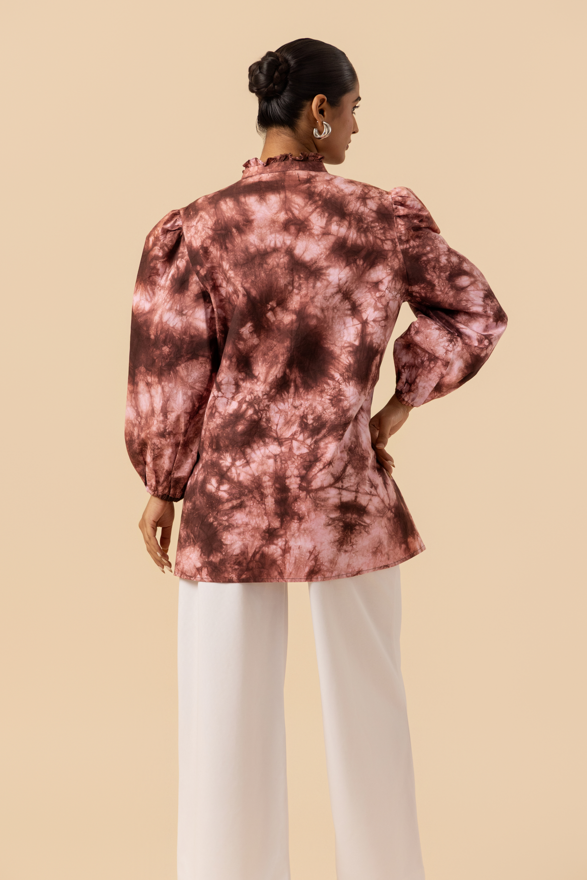 Back view of a model wears a vibrant brown tie-dye shirt dress with puffed sleeves, paired with white wide-leg trousers and stylish sandals.