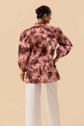 Back view of a model wears a vibrant brown tie-dye shirt dress with puffed sleeves, paired with white wide-leg trousers and stylish sandals.