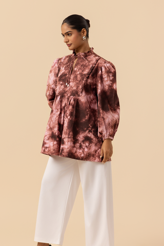 Side view of a model wears a vibrant brown tie-dye shirt dress with puffed sleeves, paired with white wide-leg trousers and stylish sandals.