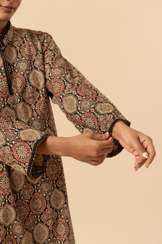 Closeup view of a woman's hand wearing a patterned ethnic ajrakh printed farshi co-ord set featuring a long tunic and wide-legged pants, posed against a neutral background.