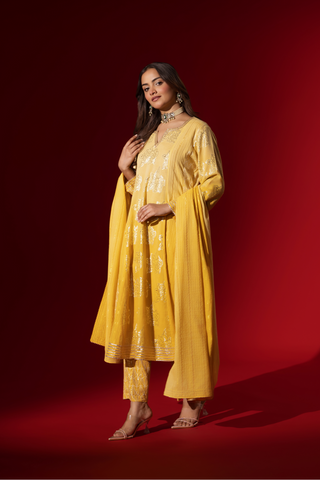 Side view of a woman showcases an elegant yellow traditional outfit with intricate designs, contrasting beautifully against a deep red background.