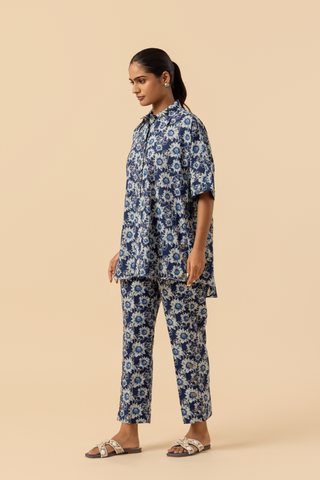 Side view of a model in a blue floral-patterned outfit stands against a soft beige background, showcasing a relaxed style.