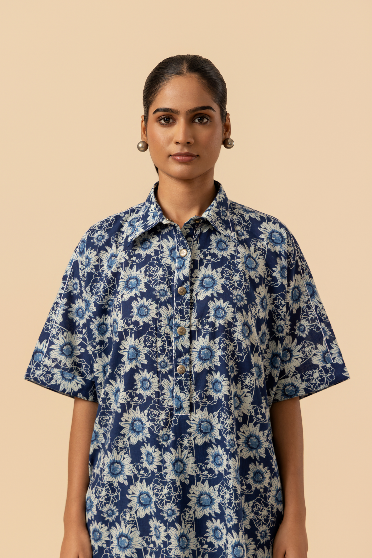 Closeup view of a view of a model in a blue floral-patterned outfit stands against a soft beige background, showcasing a relaxed style.