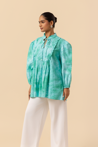 Side view of a model wears a vibrant ocean mist tie-dye shirt dress with puffed sleeves, paired with white wide-leg trousers and stylish sandals.