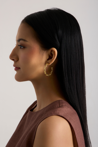 A woman in profile wearing a textured gold hoop earring, shown against a plain light gray background.