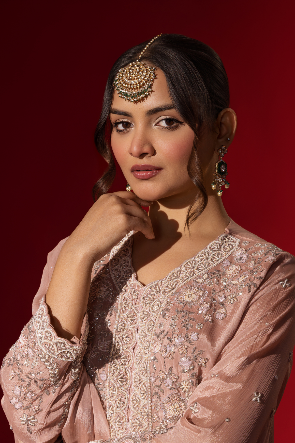 Closeup view of a woman wears an elegant pastel pink embroidered kurta set with intricate beadwork, standing against a vibrant red background.