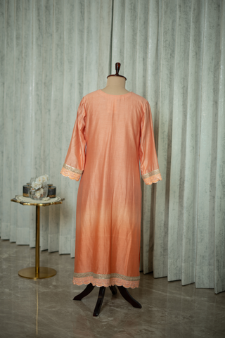 Back view of a peach silk kurta with intricate embroidery on display, featuring elegant sleeves and neckline detailing, set against a modern backdrop.