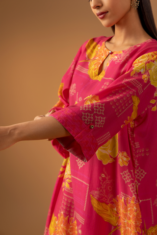 Closeup view of a model showing her hand in a vibrant pink floral co-ord set with matching pants, set against a warm neutral background. 