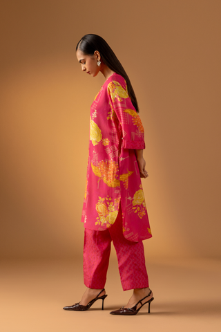 Side view of a model showcases a vibrant pink floral co-ord set with matching pants, set against a warm neutral background. 