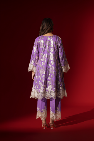 Back view of a woman poses in a purple ethnic  shimmer kurta set outfit with intricate white embroidery against a vibrant red backdrop.