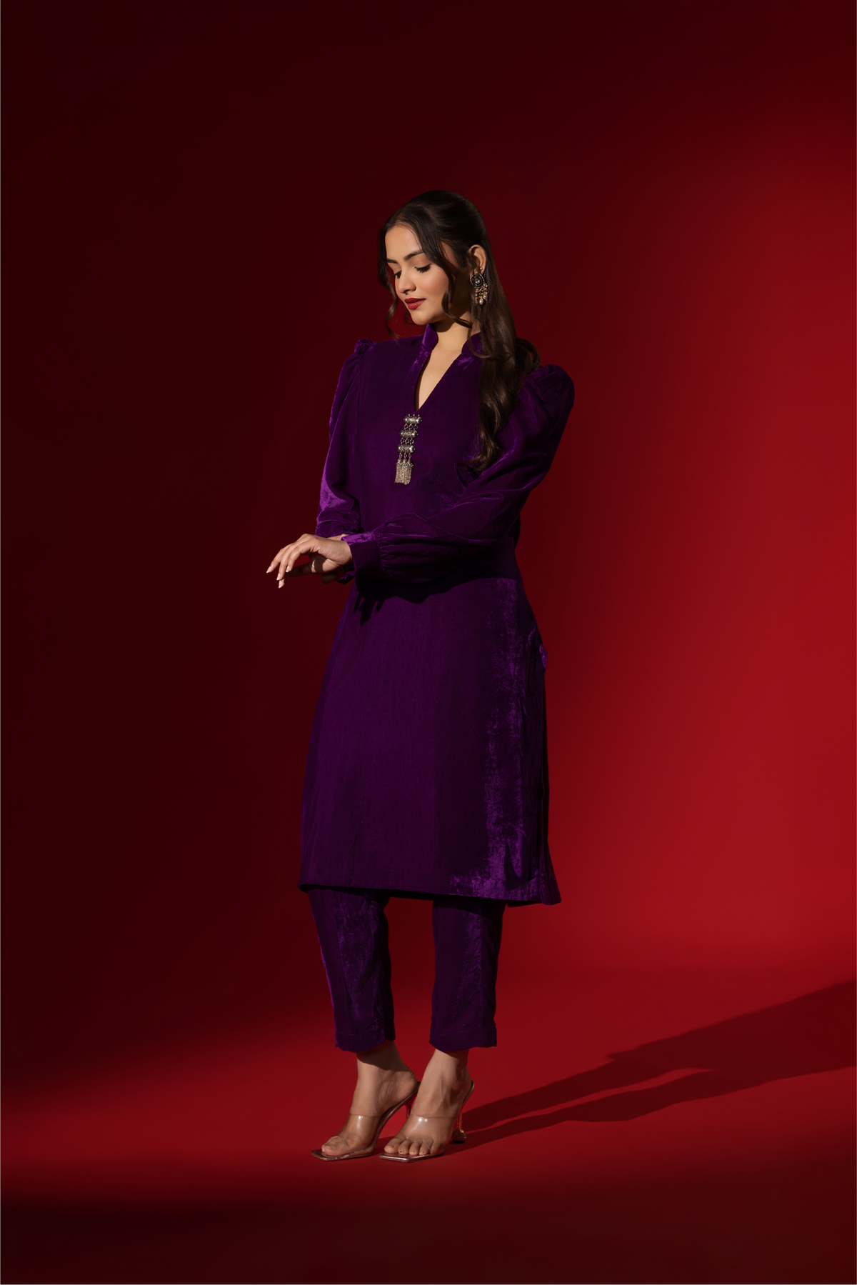 Side view of a woman in a vibrant purple velvet co-ord set with a feminine silhouette and elegant earrings, set against a rich red background.