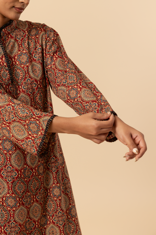 Closeup view of a model's hand wearing a patterned brown ajrakh print co-ord set and against a beige background, emphasizing traditional ethnic wear.