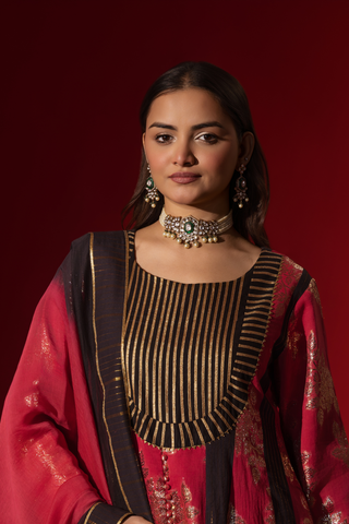 Closeup view of a model poses in a vibrant red and black traditional outfit, adorned with intricate patterns and complemented by elegant jewelry.