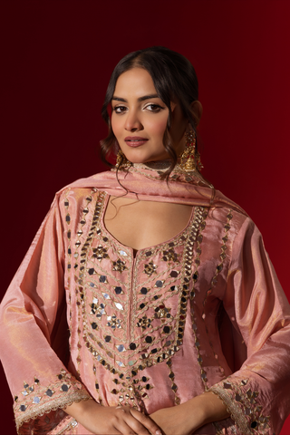 Closeup view of a  woman stands elegantly in a rose embroidered kurta set with intricate patterns, complemented by a matching dupatta against a bold red background.
