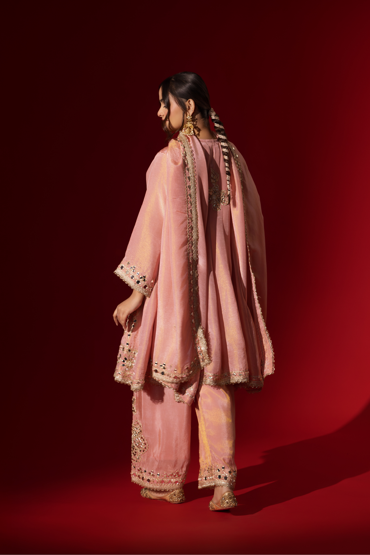 Back view of a woman stands elegantly in a rose embroidered kurta set with intricate patterns, complemented by a matching dupatta against a bold red background.