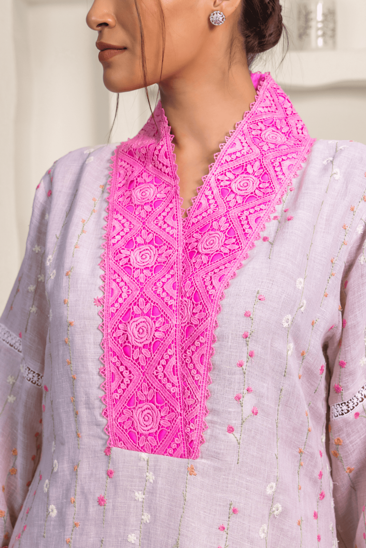 Closeup view of model wearing a light lavender kurta adorned with vertical embroidery patterns and bright pink lace detailing on the collar and cuffs.