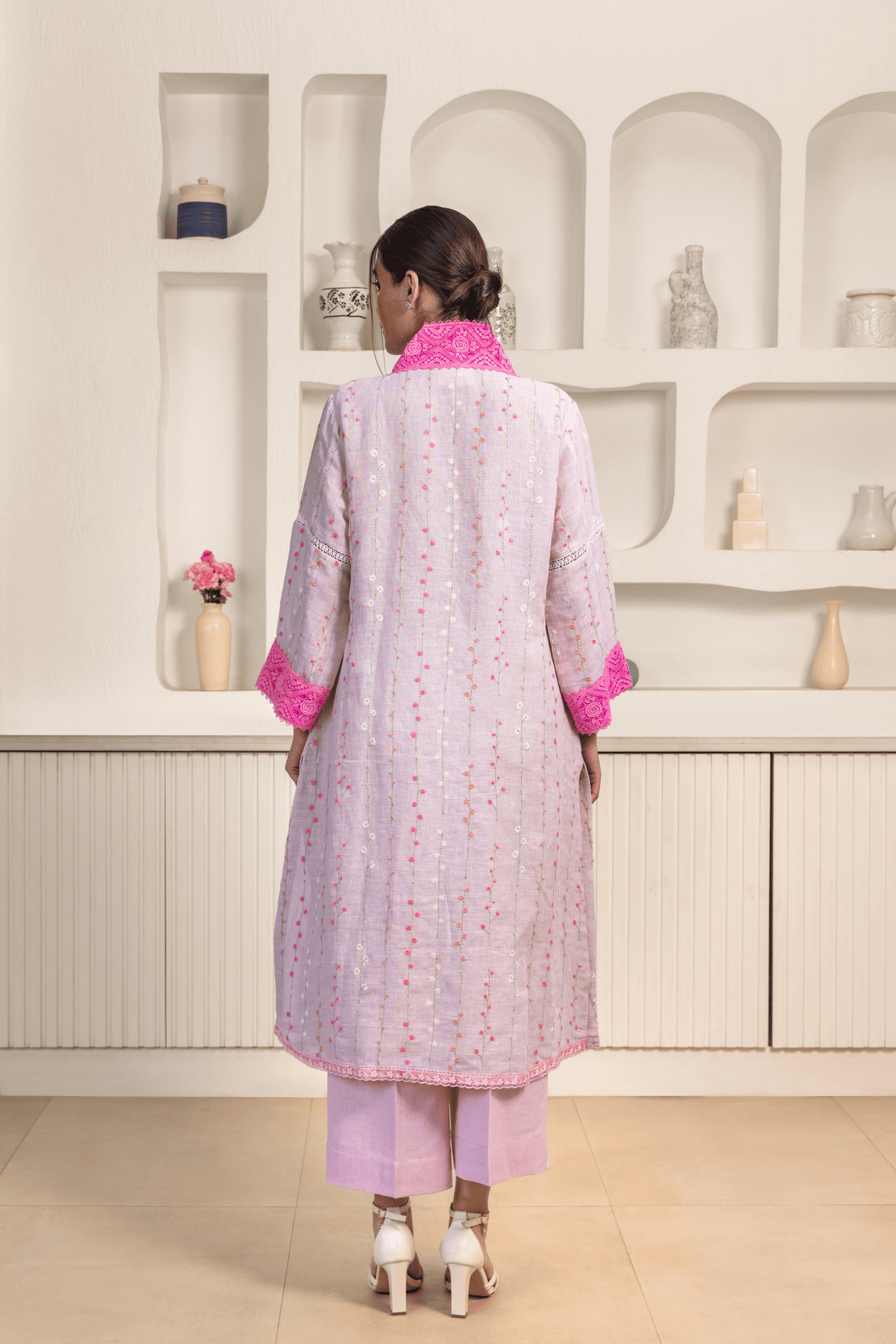 Back view of model is dressed in a light lavender kurta adorned with vertical embroidery patterns and bright pink lace detailing on the collar and cuffs.