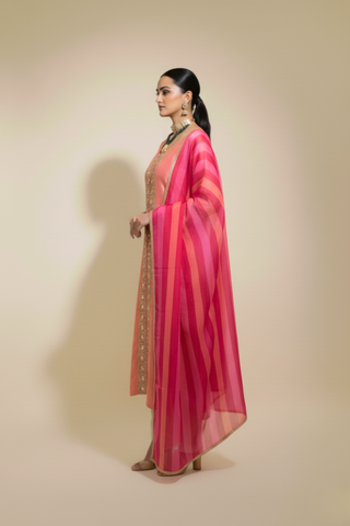 Side view of a woman wears a traditional pink tissue chanderi kurta set adorned with intricate embellishments, paired with a light pink dupatta and beige trousers.