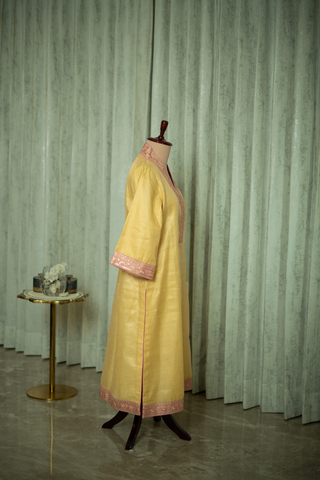 Side view of a vibrant yellow kurta with pink accents and a matching dupatta draped elegantly on a mannequin against a soft green backdrop.