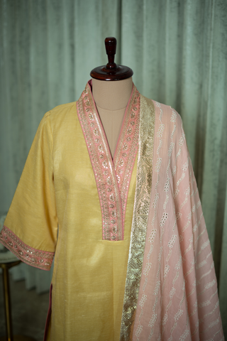 Closeup view of a vibrant yellow kurta with pink accents and a matching dupatta draped elegantly on a mannequin against a soft green backdrop.