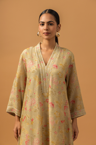 Closeup view of a woman in a floral-patterned, long beige linen co-ord set and striped pants stands against a warm beige background.