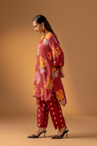 Side view of a model wears a vibrant floral co-ord set over matching patterned pants, set against a warm, neutral backdrop.