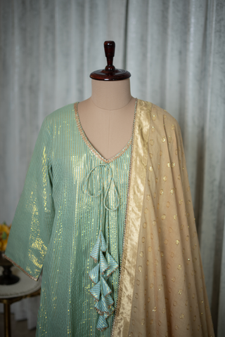 Closeup view of a mint green kurta with gold detailing and golden dupatta, featuring delicate tassel accents, displayed elegantly in a modern setting