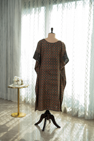 Back view of a patterned kaftan dress with short sleeves displayed on a mannequin in a sunlit room.