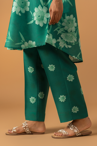 Close-up view of a woman wearing in a vibrant green floral co-ord set, featuring a loose shirt and matching pants, complemented by embellished sandals.