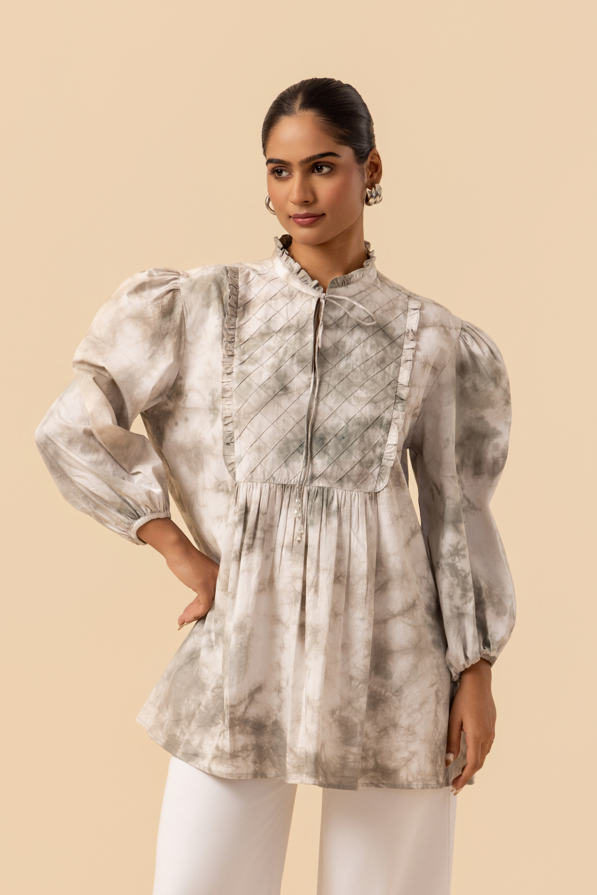 Closeup side view of a model wears a vibrant white & grey tie-dye shirt dress with puffed sleeves, paired with white wide-leg trousers and stylish sandals.
