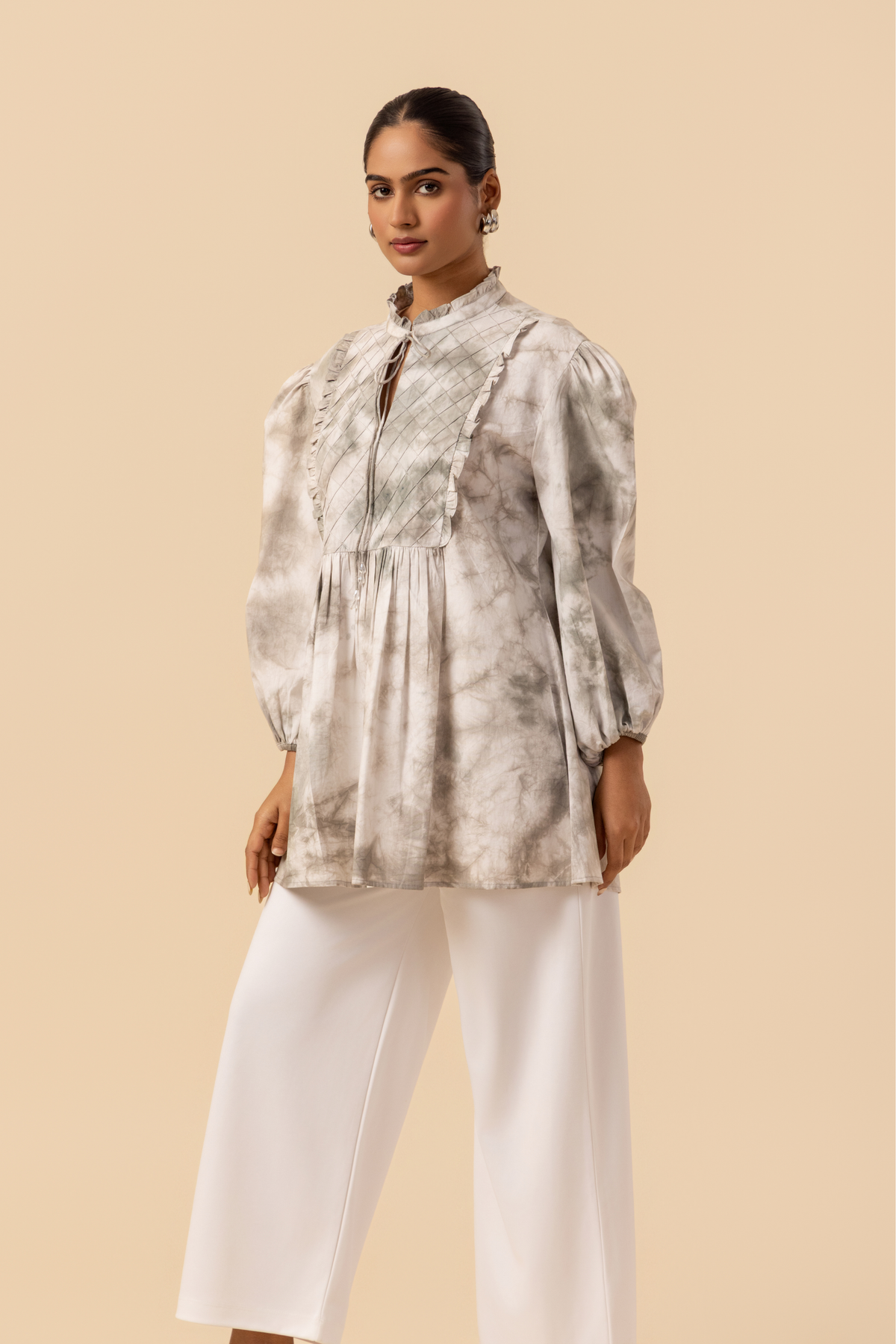 Side view of a model wears a vibrant white & grey tie-dye shirt dress with puffed sleeves, paired with white wide-leg trousers and stylish sandals.