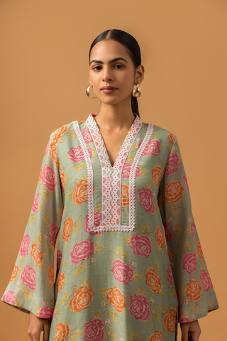 Closeup view of a model stands in a vibrant spring rose floral co-ord set with intricate neckline embroidery, paired with striped pants on a warm, neutral background.