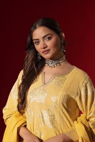 Closeup view of a woman showcases an elegant yellow traditional outfit with intricate designs, contrasting beautifully against a deep red background.