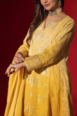 A close-up of a woman's hand showcases an elegant yellow traditional outfit with intricate designs, contrasting beautifully against a deep red background.