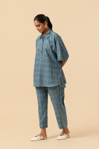 Side view of a person in a patterned blue matching outfit stands confidently against a neutral background, showcasing their unique style.
