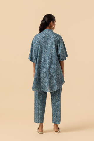 Back view of a person in a patterned blue matching outfit stands confidently against a neutral background, showcasing their unique style.