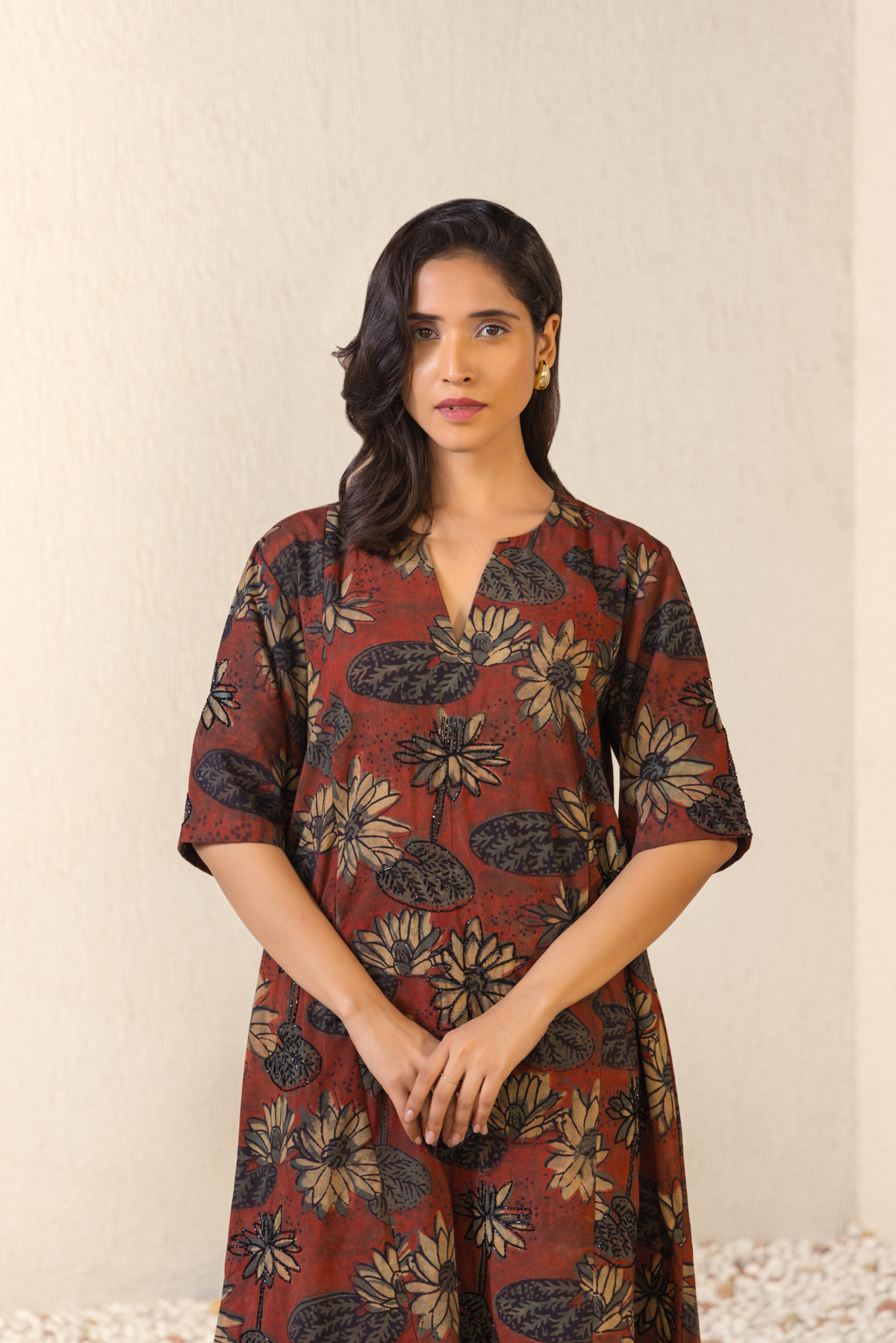 Closeup View of a woman dressed in a maroon floral linen kurta set with coordinated pants, styled against a serene outdoor archway backdrop