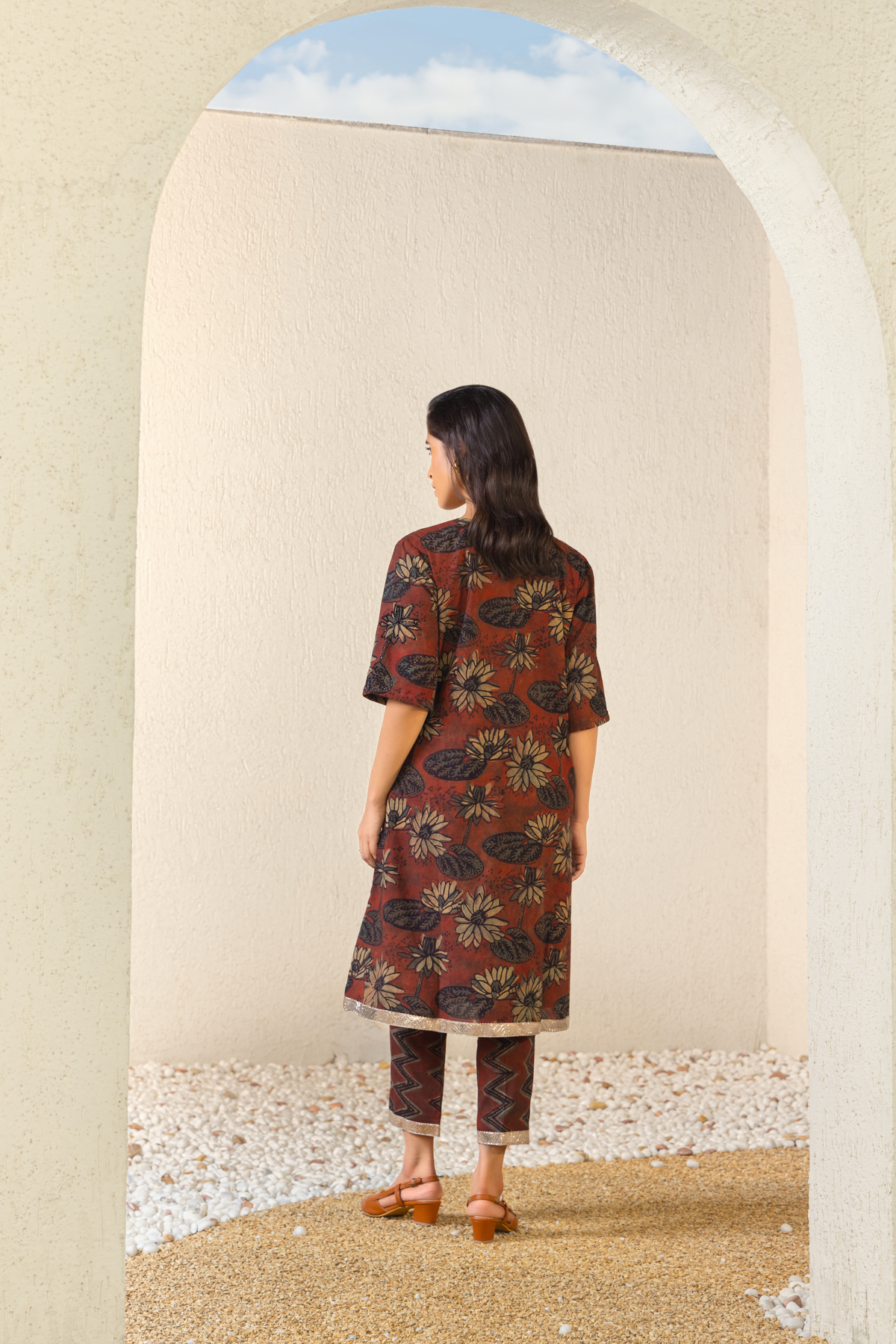 Back View of a woman dressed in a maroon floral linen kurta set with coordinated pants, styled against a serene outdoor archway backdrop