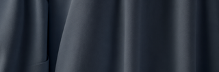 A close-up of draped dark blue-gray fabric with soft folds and a smooth matte texture.