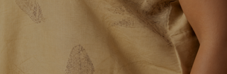 A close-up of a beige fabric with a subtle brown leaf pattern, draped with a person's arm visible on the right side.
