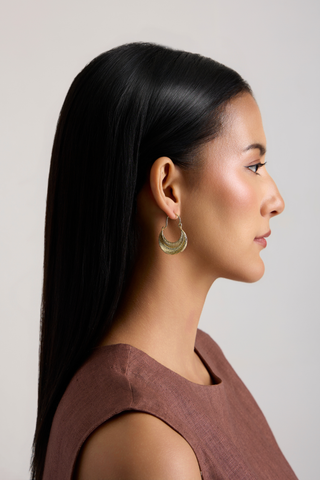 A woman in profile wearing a pair of layered gold crescent moon earrings, shown against a neutral light gray background.