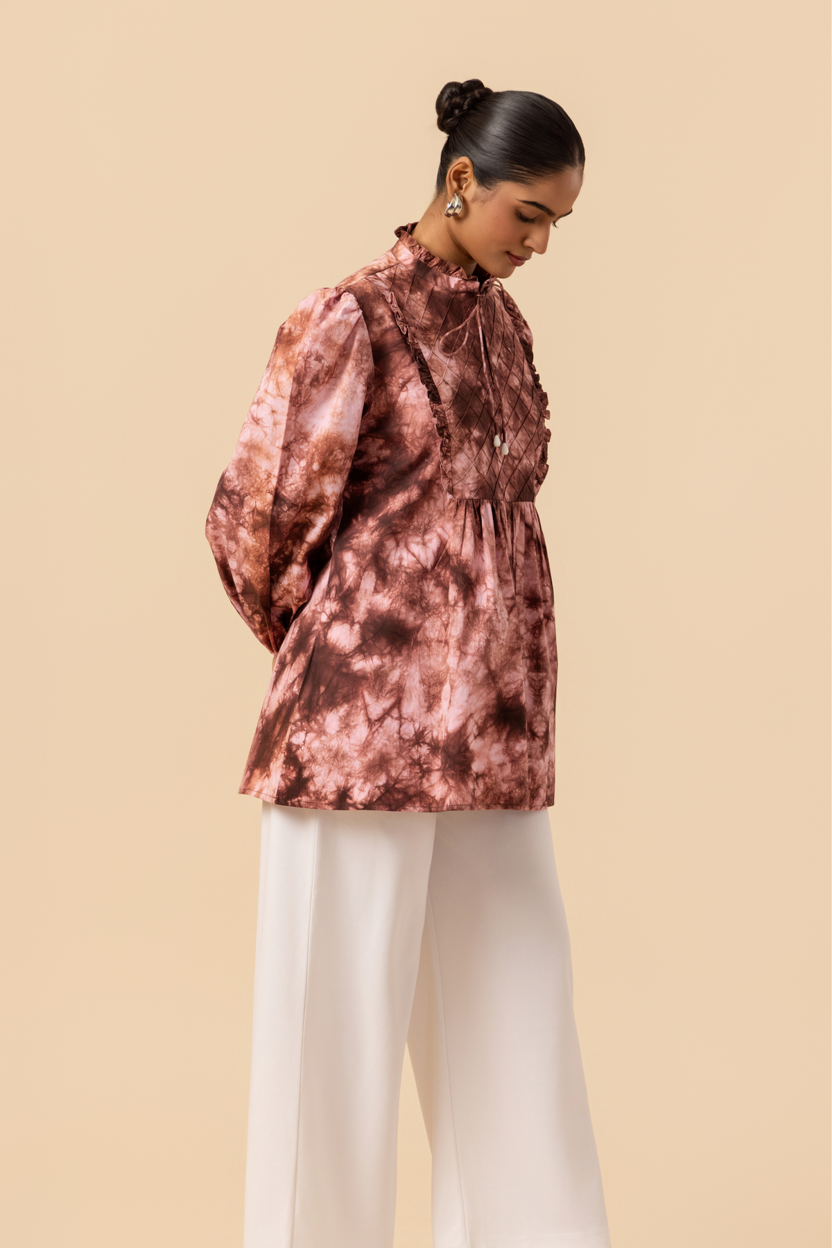 Right side view of a model wears a vibrant brown tie-dye shirt dress with puffed sleeves, paired with white wide-leg trousers and stylish sandals.