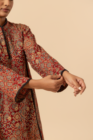 Closeup view of a model's hand wearing a vibrant, patterned ethnic ajrakh printed farshi co-ord set featuring a long tunic and matching pants in rich red tones.
