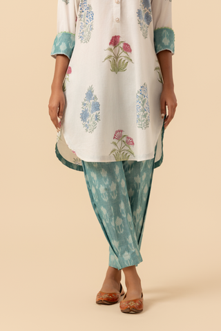 A person stands wearing a floral-printed tunic and teal pants cotton co-ord set, set against a soft beige background against a neutral backdrop.