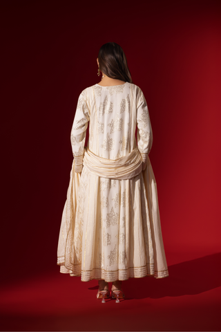 Back view of a woman showcases an elegant white anarkali kurta set with intricate designs, contrasting beautifully against a deep red background.