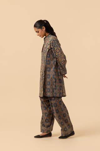 Side view of a model wearing a long, patterned ajrakh print co-ord set which has tunic and loose pants, showcasing intricate designs in dark blues and golds against a neutral background.