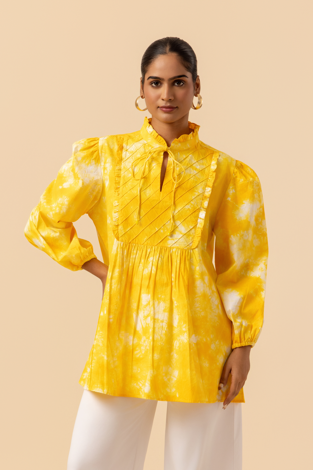 Closeup view of a woman wears a vibrant yellow tie-dye shirt dress with puffed sleeves, paired with white wide-leg trousers and stylish sandals.