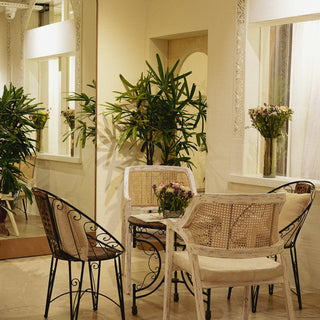 Cozy interior featuring a round table with wicker chairs, surrounded by lush plants and vases of fresh flowers in a well-lit space.