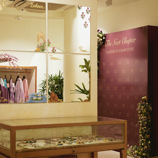 Interior of Naseeboo flagship store featuring colorful kurta sets, plants, and a display case of jewelry against a chic backdrop.
