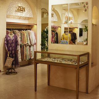 A boutique interior featuring colorful clothing on racks, a display case with jewelry, and a mirror adorned with flowers.